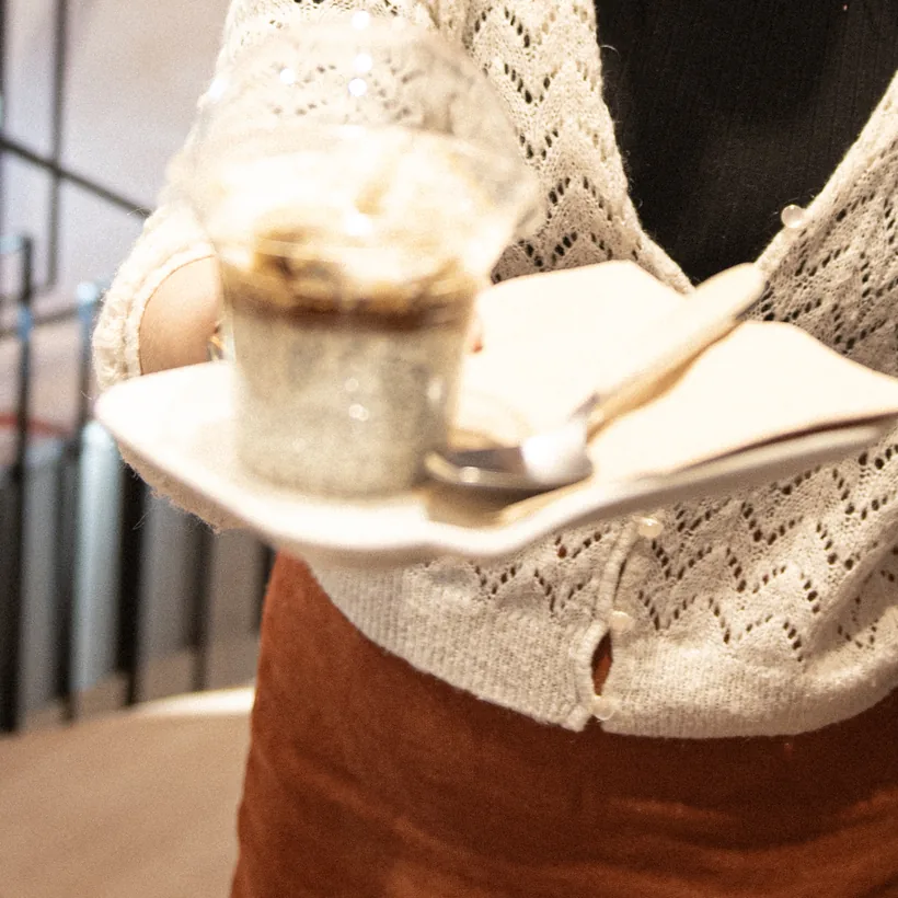 A breakfast cup on a plate, with a spoon, on its way to a table