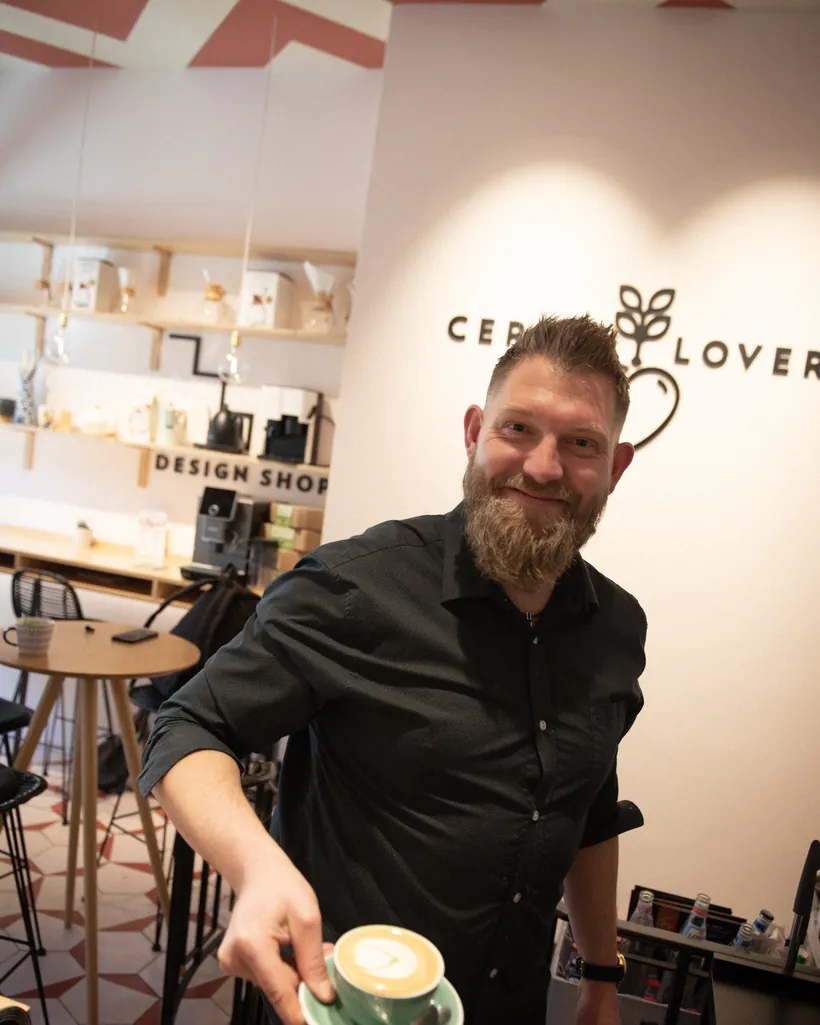 A barista smiling, holding out a flat white