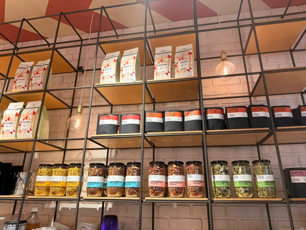 The shelf wall: coffee bags above rows of gold, turquoise, pink and green granola jars